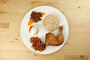 Indonesian royal dish nasi bojari with deep spiced deep fried chicken leg sambal prawn curry beef rendang boild egg cucumber and tomato slice photo