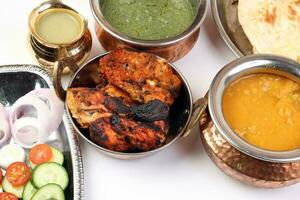 Spicy red Chicken grilled tikka tandoori nan bread green spinach curry yogurt sauce dal tomato cucumber onion salad set in metal stainless steel brass copper pot on white background photo