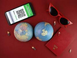 Vaccine passport smartphone app red sunglass world atlas globe map north south pole on red paper background world travel tour vacation mini human figures photo