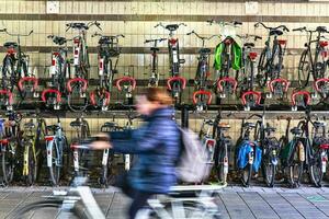 bicycles parked and a lady riding one on the ground floor. photo