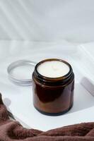 White aroma candle in glass jar with wooden wick on white background with books and cloth photo