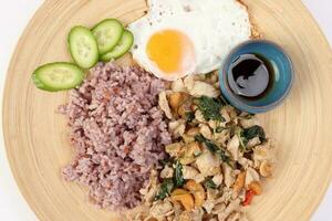 Thai fusion stair fried chicken with Thai basil and cashew nut with health brown rice fried egg sauce cucumber on woody plate over white background photo