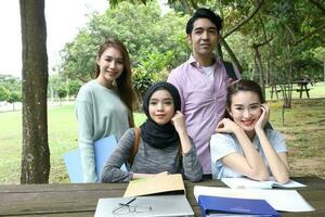 joven asiático malayo chino hombre mujer al aire libre parque libro archivo carpeta ordenador portátil computadora teléfono sentar estar estudiar mezclarse foto