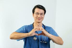 Young Asian male doctor wearing apron uniform tunic stethoscope look at camera hart hand sing photo