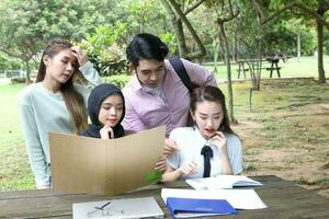 joven asiático malayo chino hombre mujer al aire libre parque libro archivo carpeta ordenador portátil computadora teléfono sentar estar estudiar mezclarse foto