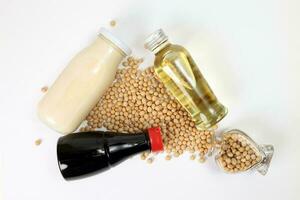 Soyabeans pouring from hart shape glass bottle around bottle of soya bean milk oil sauce on white background photo