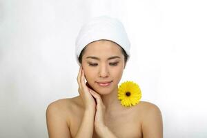 Young beautiful Southeast Asian woman beauty fashion makeup light grey white background towel rapped on head hand finger on face yellow flower on shoulder eyes closed photo