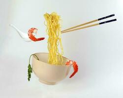 Yellow seafood prawn coriander leaf noodle soup elevated flying suspended in air with soup spoon and chopstick on white background photo