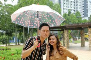 Young Asian Malay man woman outdoor green park walk talk discuss mingle under umbrella photo