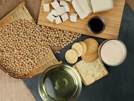 Soyabeans products soya beans flowing bamboo sieve wooden board on jute black stone slate background curd tofu oil milk sauce biscuit cookies photo