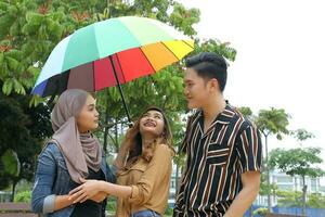 Young Asian Malay man woman outdoor green park walk talk discuss mingle under umbrella photo