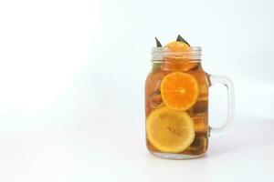 Liquid ice lemon orange tea with slice green leaf cinnamon stick in transparent glass jar mug on white background photo