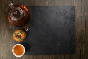 Colourful flower decorated mooncake cut slice half layer Chinese mid autumn festival on glass teapot white ceramic teacup over black slate stone border copy text space photo