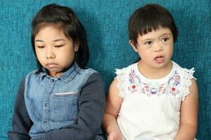 Two little south east Asian girl child malay Chinese study play draw use smart phone on blue fabric sofa they are autistic and down syndrome photo