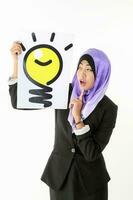 South East Asian young Malay woman wearing formal business office ware headscarf on white background holding idea light bulb sign photo