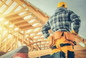 Carpentry Construction Worker in Front of Newly Developed Wooden Skeleton House Frame photo