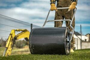 Landscaper Pushing Grass Roller to Compact New Turfs in a Backyard Garden photo