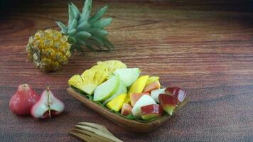 Sliced Fruit Salad, in Indonesia known as Rujak Buah or Lutis or Lotis. Served with Spicy Brown Sugar sauce and Ground Peanuts in a plate on wood background with hand video