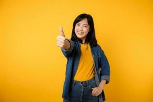 Portrait young happy asian woman cheerful smile showing thumb up, trust, recommend gesture isolated on yellow studio background. Pretty attractive female with like hand sign. lifestyle girl woman photo