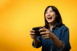 Portrait young asian woman with happy success smile wearing denim clothes holding joystick controller and playing video game. Fun and relax hobby entertainment lifestyle concept. photo