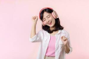 Smile pretty asian model person listen music song and enjoy dance with wireless headphone online audio radio sound. Positive fun exited joyful youth female woman on pink isolated background studio photo