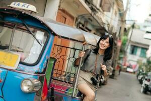 Young Asian woman backpack traveler standing a side of Tuk Tuk taxi on summer vacations at Bangkok, Thailand. photo