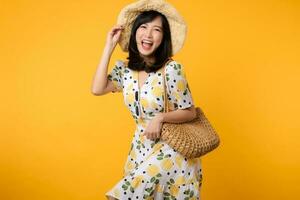 Portrait happy attractive young asian woman with trendy springtime dress, hat, sunglasses fashion and woven bag isolated on yellow background. Summertime sale shopping concept. photo