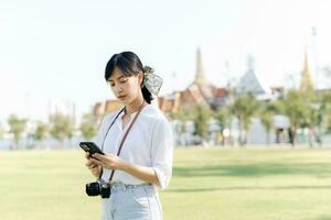Portrait beautiful young asian woman with smartphone on summer holiday vacation trip with the grand palace in a background at Bangkok, Thailand photo