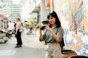 Young Asian woman backpack traveler using digital compact camera, enjoying street cultural local place and smile. Traveler checking out side streets. photo