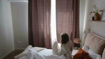 caucasico donna veglia su nel sua letto nel il mattina. giovane del Millennio donna fare sua mattina routine a il Camera da letto video