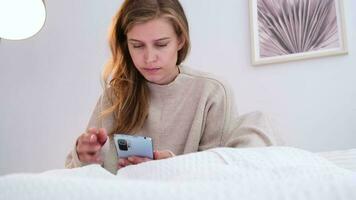 mulher sentado às cama às lar, tendo café da manhã e usando Smartphone. jovem milenar mulher fazendo dela manhã rotina às a quarto video