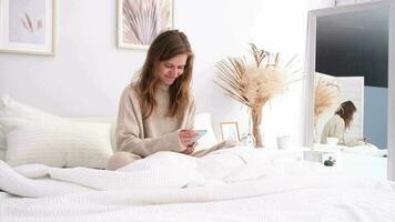 Woman sitting at bed at home, having breakfast and using smartphone. young millennial woman doing her morning routine at the bedroom video