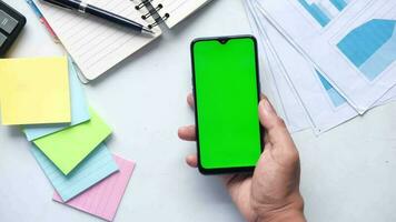 Jeune homme tenir une intelligent téléphone avec vert écran avec bloc-notes et stylo sur table video