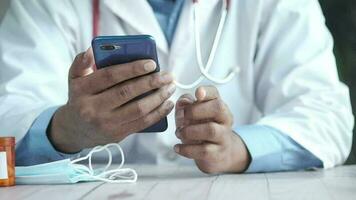 médecin dans blanc manteau en utilisant une téléphone intelligent tandis que séance video