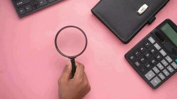 Hand holding magnifying glass against pink background video