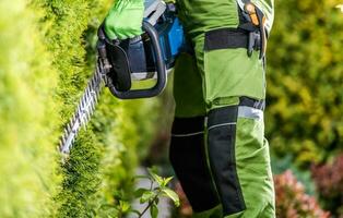 profesional jardinero con cobertura recortadora haciendo su trabajo en el jardín foto