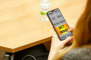 Close up cropped shot of female hands holding smartphone with bookmaker's website on a screen. Young woman placing sport bets online using mobile application. photo