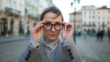 portrait de une caucasien femme dans une manteau permanent dans le milieu de le vieux ville carré. elle regards à le caméra et met sur des lunettes video