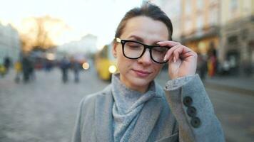 portrait de une caucasien femme dans une manteau permanent dans le milieu de le vieux ville carré. elle regards à le caméra et met sur des lunettes video