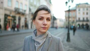 Portrait of a Caucasian woman in a coat in the middle of the old city square. She looking seriously at the camera. video