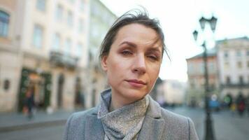 Portrait of a Caucasian woman in a coat in the middle of the old city square. She looking seriously at the camera. video