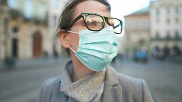 Pandemic protection of the Covid-19 coronavirus. Portrait of a woman in a coat, glasses and a protective medical mask. Glasses fog up from breath video