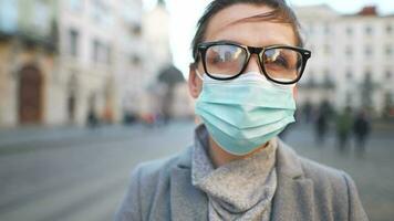 Pandemic protection of the Covid-19 coronavirus. Portrait of a woman in a coat, glasses and a protective medical mask. Glasses fog up from breath video