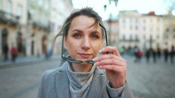 portrait de une caucasien femme dans une manteau permanent dans le milieu de le vieux ville carré. elle regards à le caméra et met sur des lunettes video