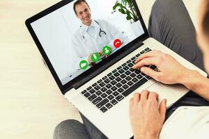 Man having video chat with doctor on laptop at home photo