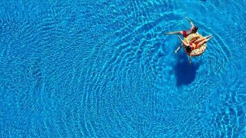 aéreo ver de hombre inmersiones dentro el el piscina mientras niña es acostado en un rosquilla piscina flotador video