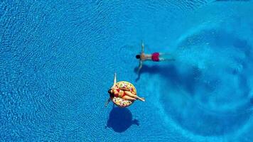 Aerial view of man dives into the the pool while girl is lying on a donut pool float video
