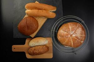 Freshly baked bread loaf bun roll round long mix verity on wooden board metal grill over black background photo