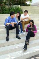 group of Asian young man woman friend student colleagues sting on stairs talk mingle discuss study book note photo