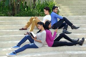 group of Asian young man woman friend student colleagues sting on stairs talk mingle discuss study book note photo